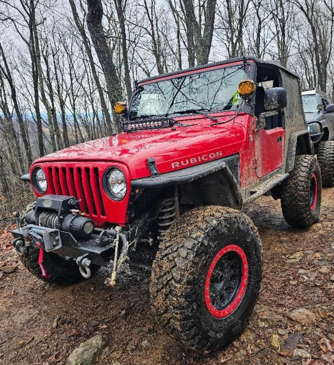 A red jeep parked on a dirt road in the woods