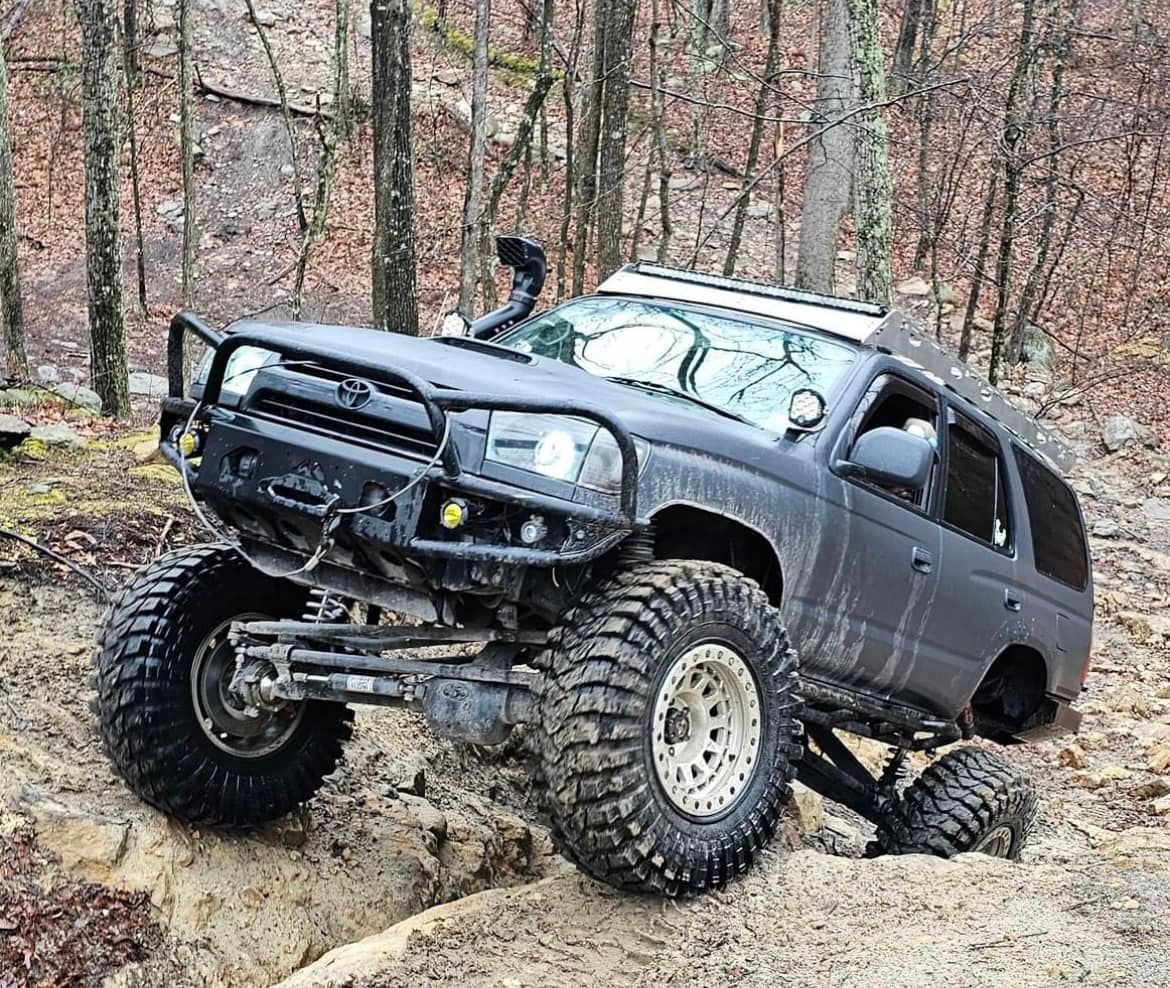A black truck driving down a dirt road in the woods