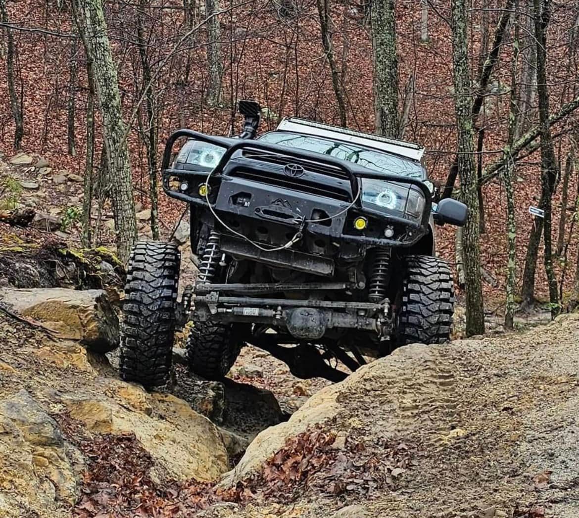 A black jeep driving down a dirt road in the woods