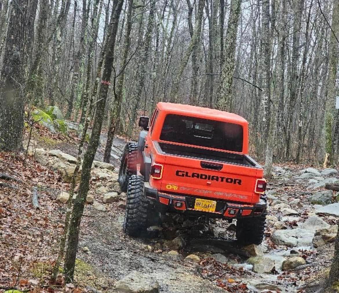 A red jeep driving down a dirt road in the woods