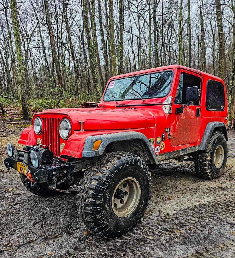 A red jeep parked on a muddy road in the woods