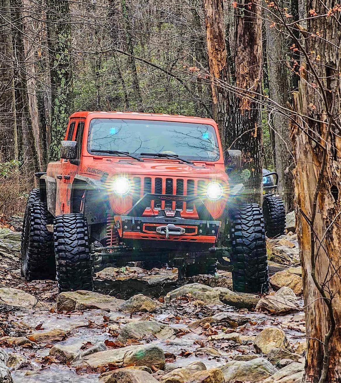 A red jeep driving through a muddy stream in the woods