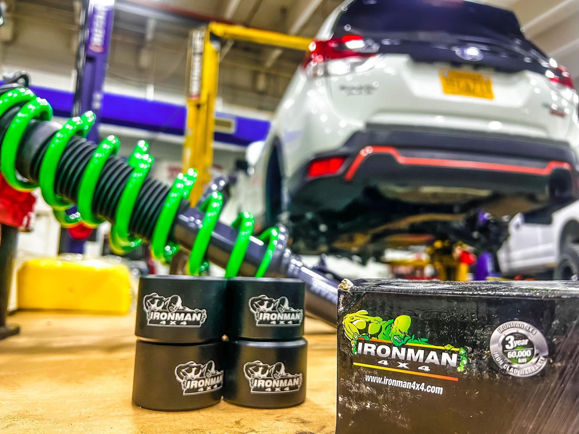 a car is sitting on a lift in a garage next to a box of ironman shock absorbers