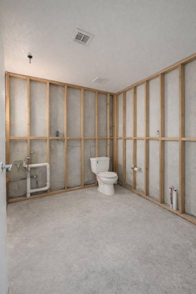 Unfinished bathroom with exposed wall studs, toilet, sink plumbing, and bare subfloor.