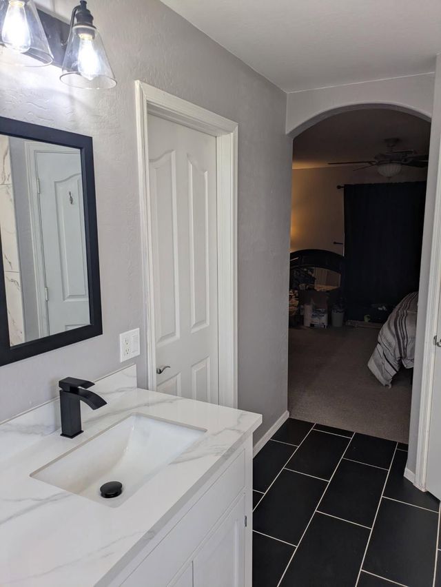 Bathroom vanity with white sink and black faucet, leading to a hallway with dark tiled floor and arched doorway