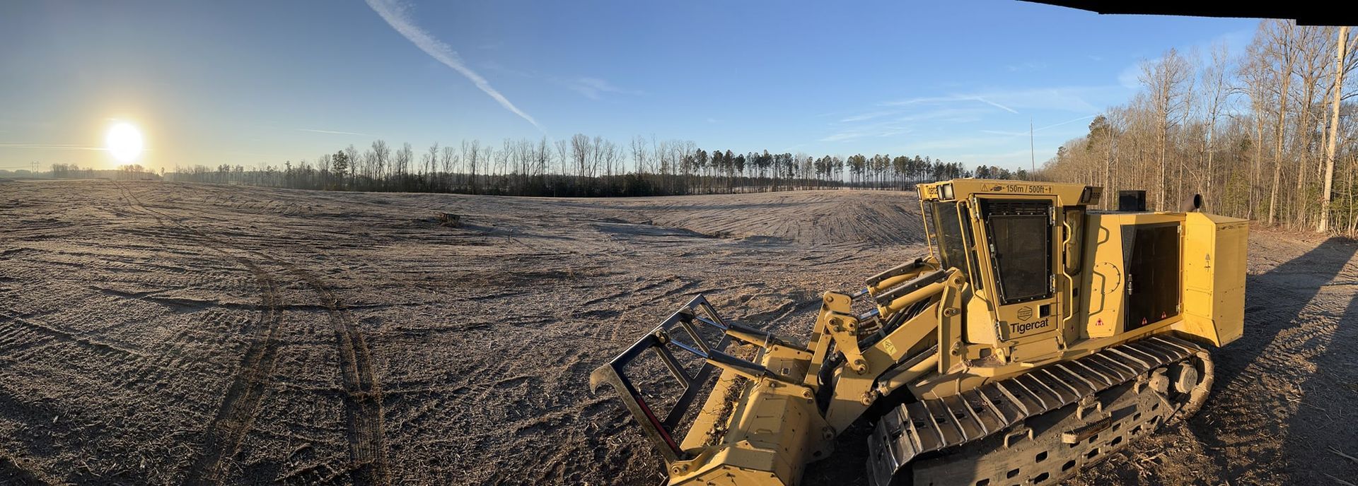 Yellow bulldozer parked on a cleared area under a bright blue sky.