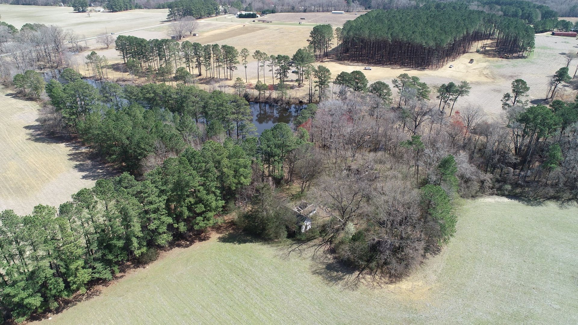 Aerial view of a rural landscape with fields, trees, and a body of water, likely a pond or creek.