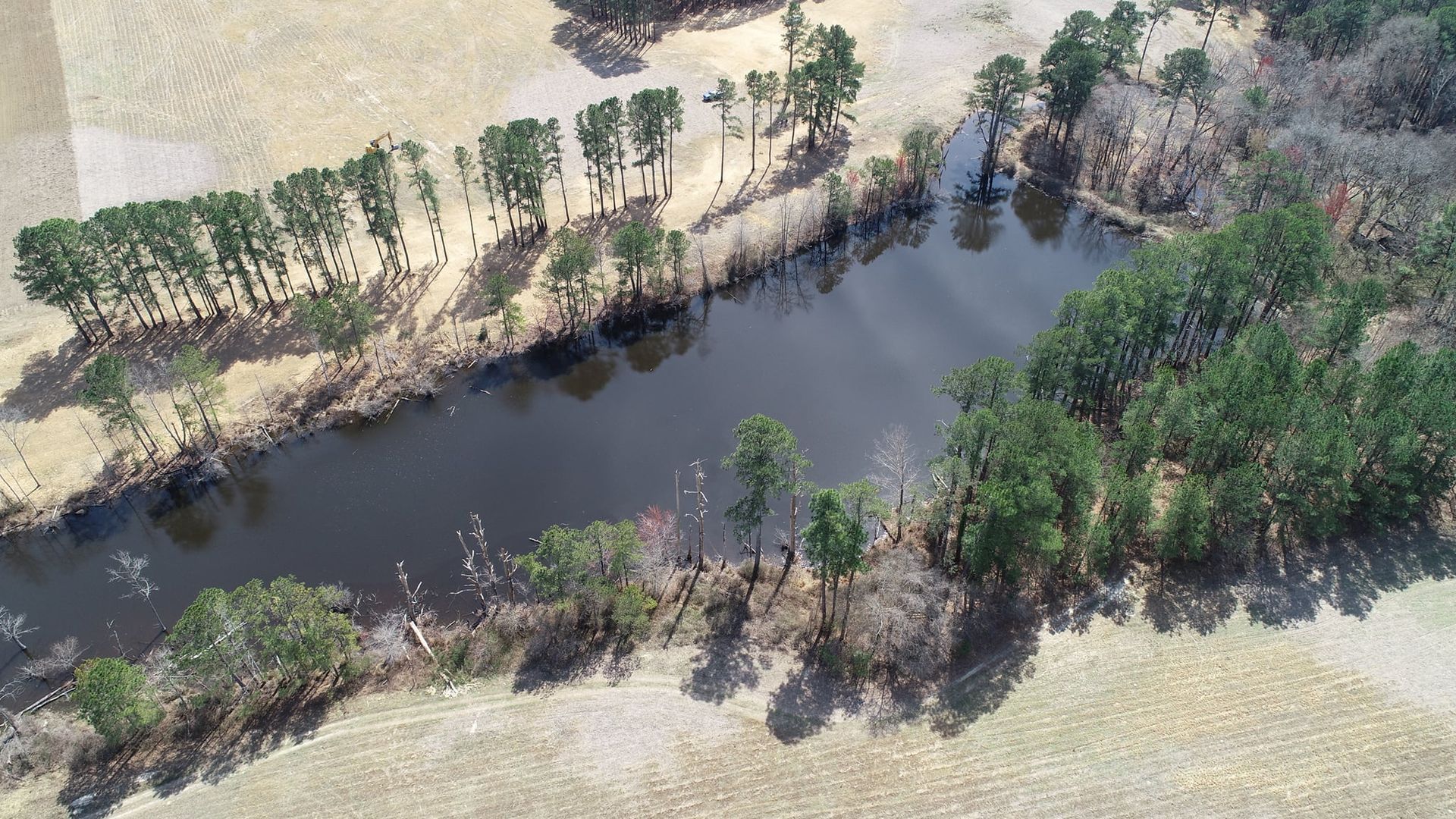 Aerial view of a dark river winding through a brown field, bordered by trees.