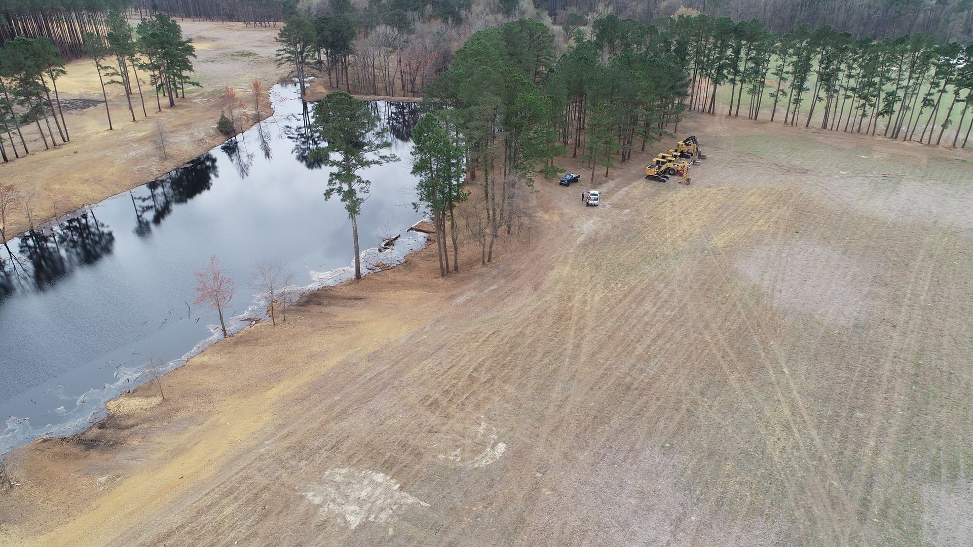 An aerial view of a brown field next to a dark body of water with trees.
