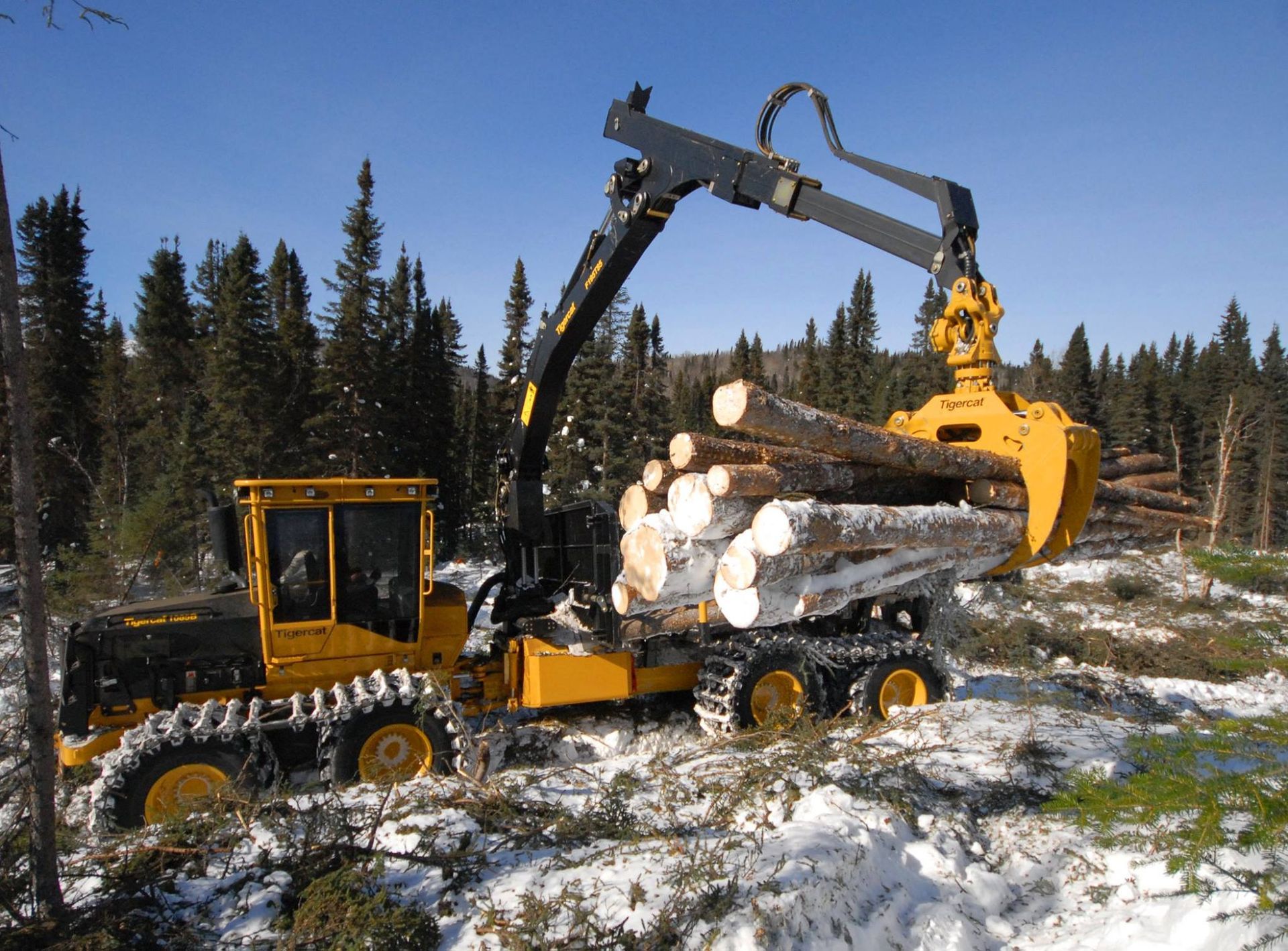 Yellow logging machine with logs in claw, operating in snowy forest.