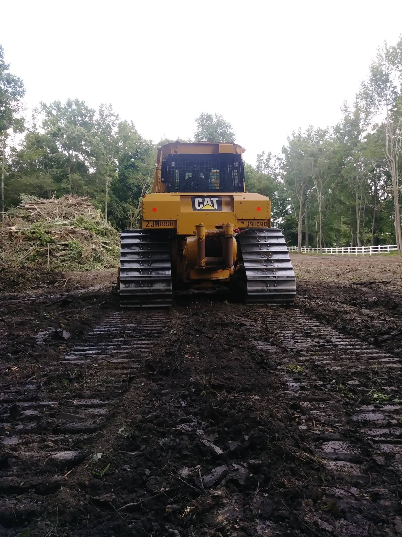 Yellow Caterpillar bulldozer on muddy ground, in a clearing with a pile of debris and trees.