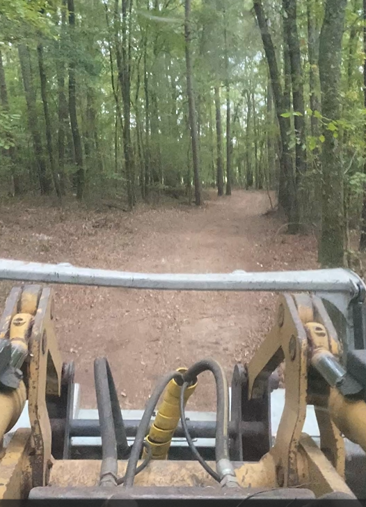 View from a skid steer looking down a dirt path through a forest.