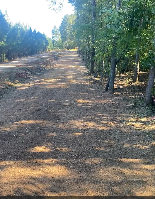 A yellow tracked machine clears brush in a field, kicking up dirt.