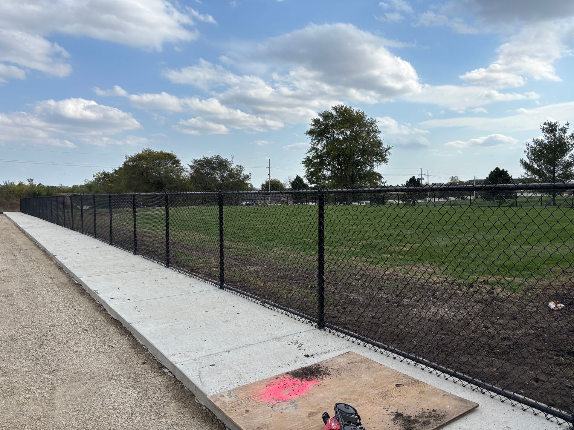 Black chain-link fence along a concrete path next to a grassy field on a cloudy day.
