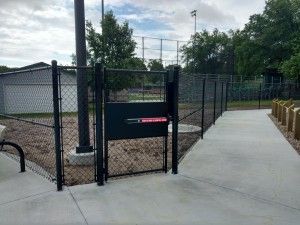 Black chain-link fence gate to a dog park with a concrete path.