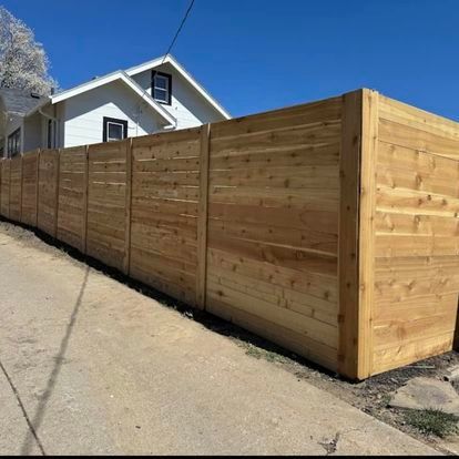 Wooden privacy fence along a concrete path next to a white house with a blue sky.