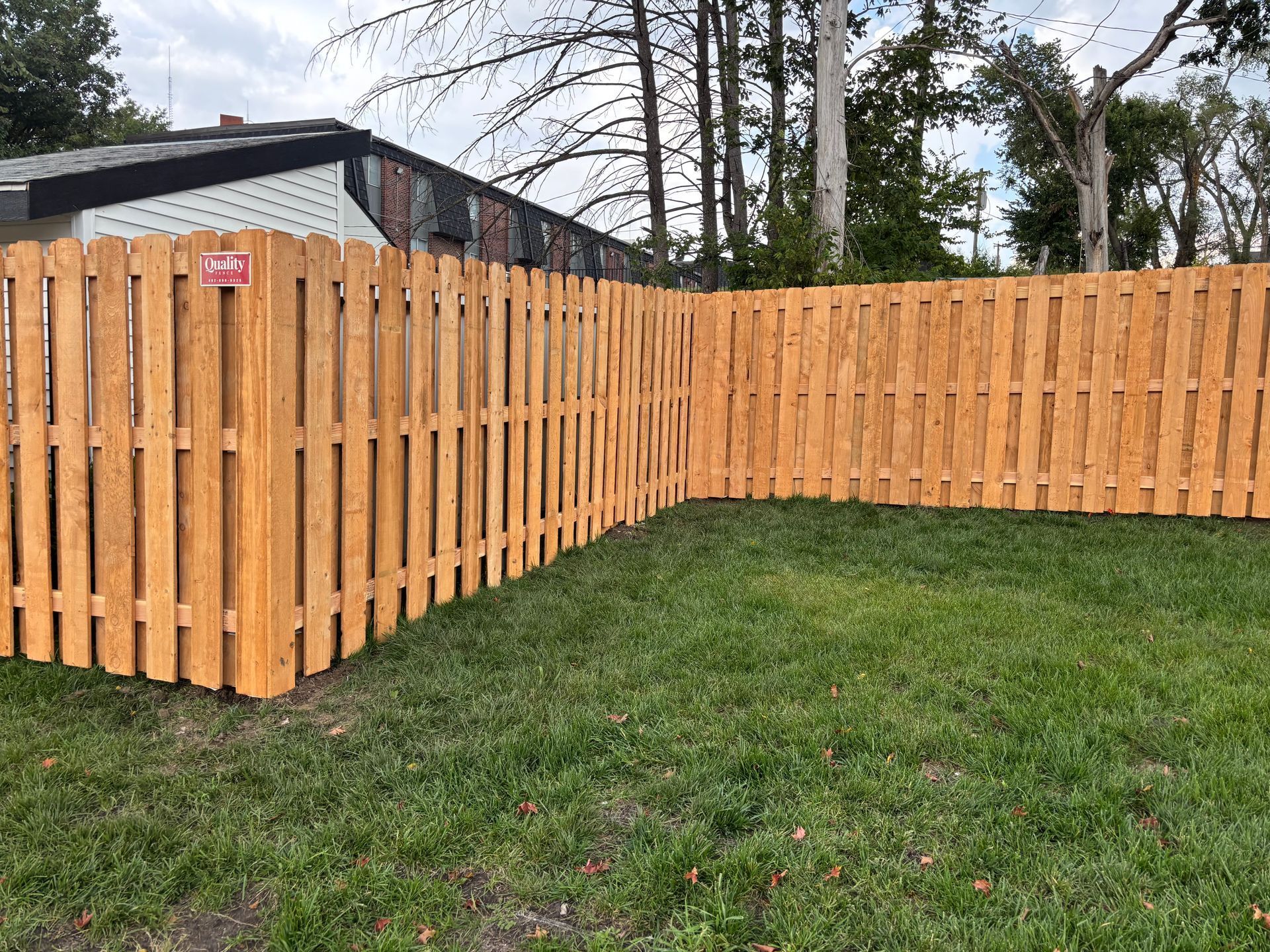 A wooden fence surrounding a grassy backyard with a house visible in the background.