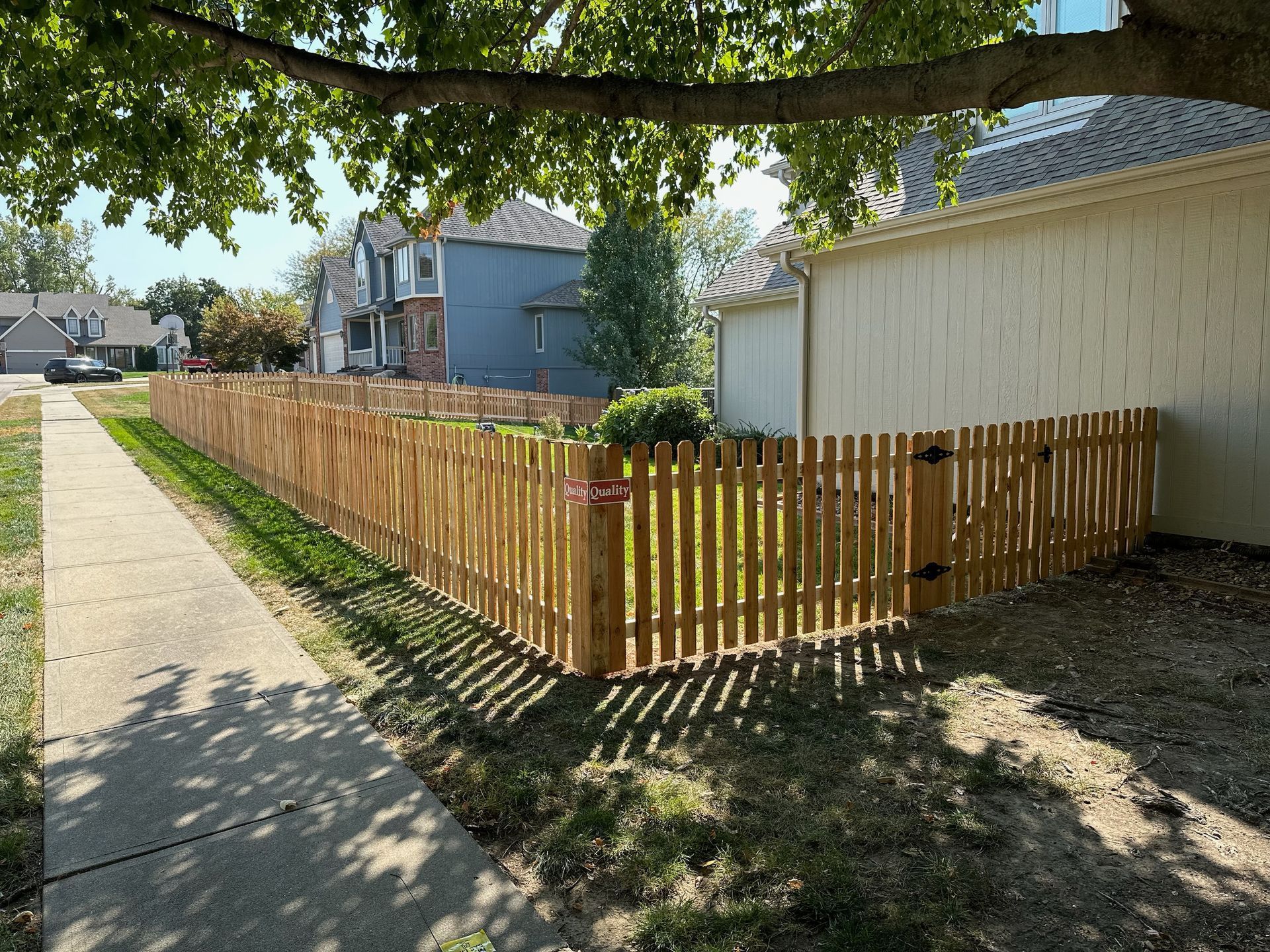 Wooden picket fence bordering a yard and sidewalk in a suburban neighborhood.