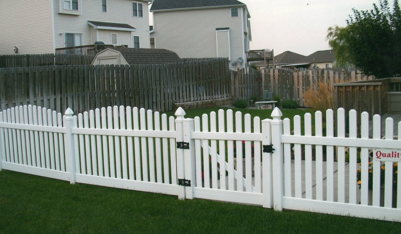 White picket fence with a gate in front of a backyard.