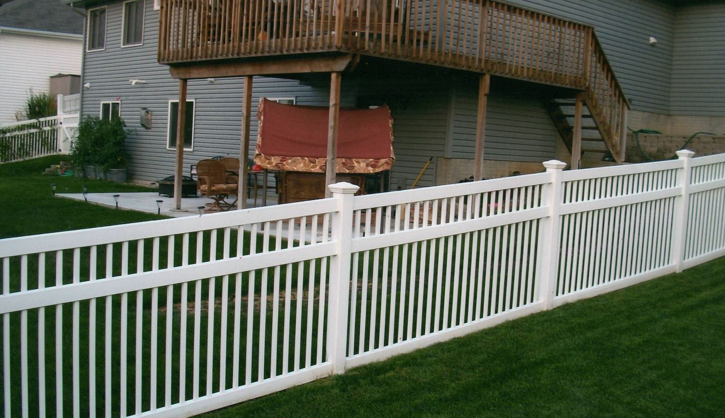 White picket fence bordering a green lawn, with a house and deck in the background.