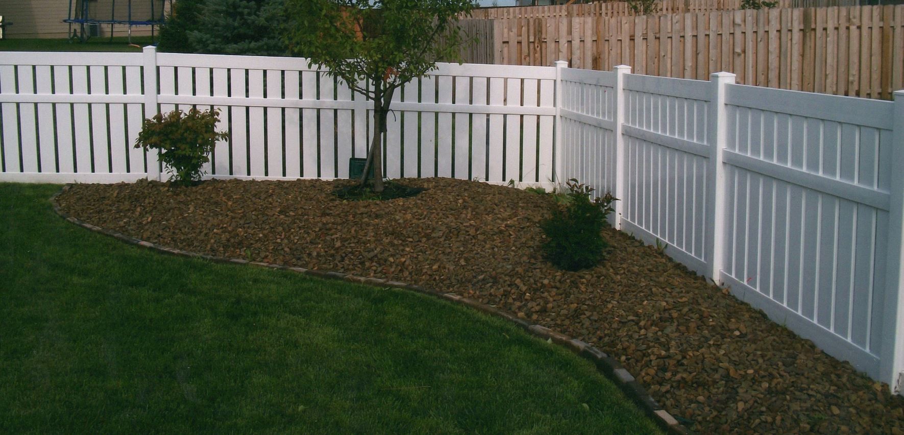 White picket fence surrounding a rock garden and green lawn, with a tree in the center.