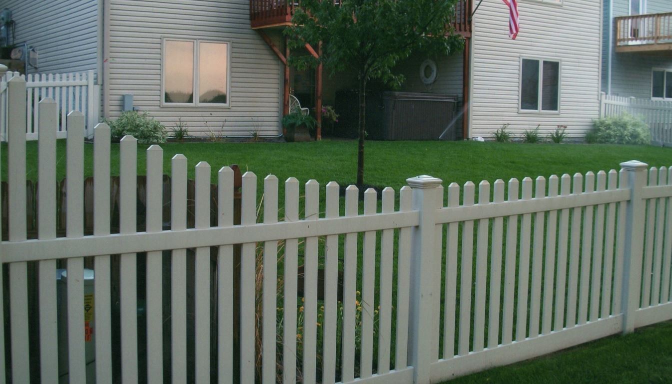 White picket fence in front of a house with a green lawn.