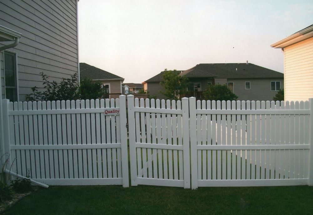 White picket fence with gate in residential backyard. Houses in background.