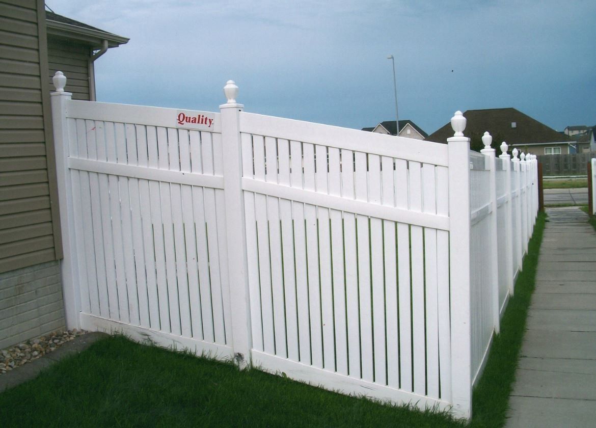 White vinyl fence along green grass and sidewalk, beside a house.