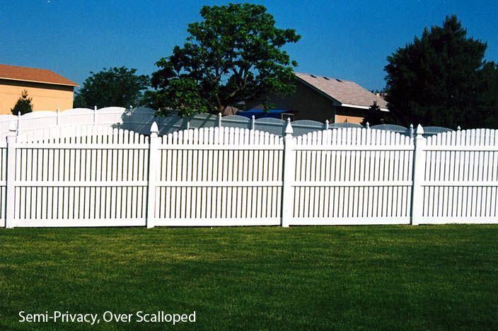 White semi-privacy, over-scalloped fence in a backyard, with houses and trees in the background.