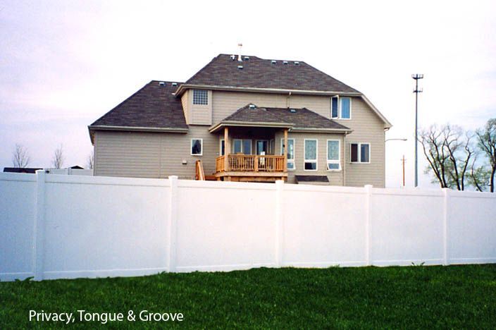White tongue and groove privacy fence surrounding a beige house with a wooden deck.