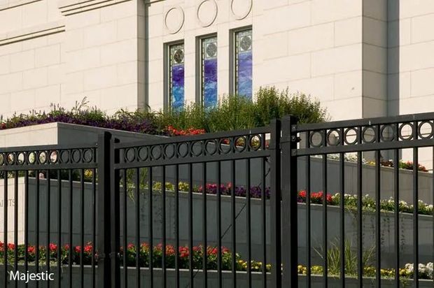 Black fence in front of a light-colored building with colorful stained glass windows and flowerbeds.