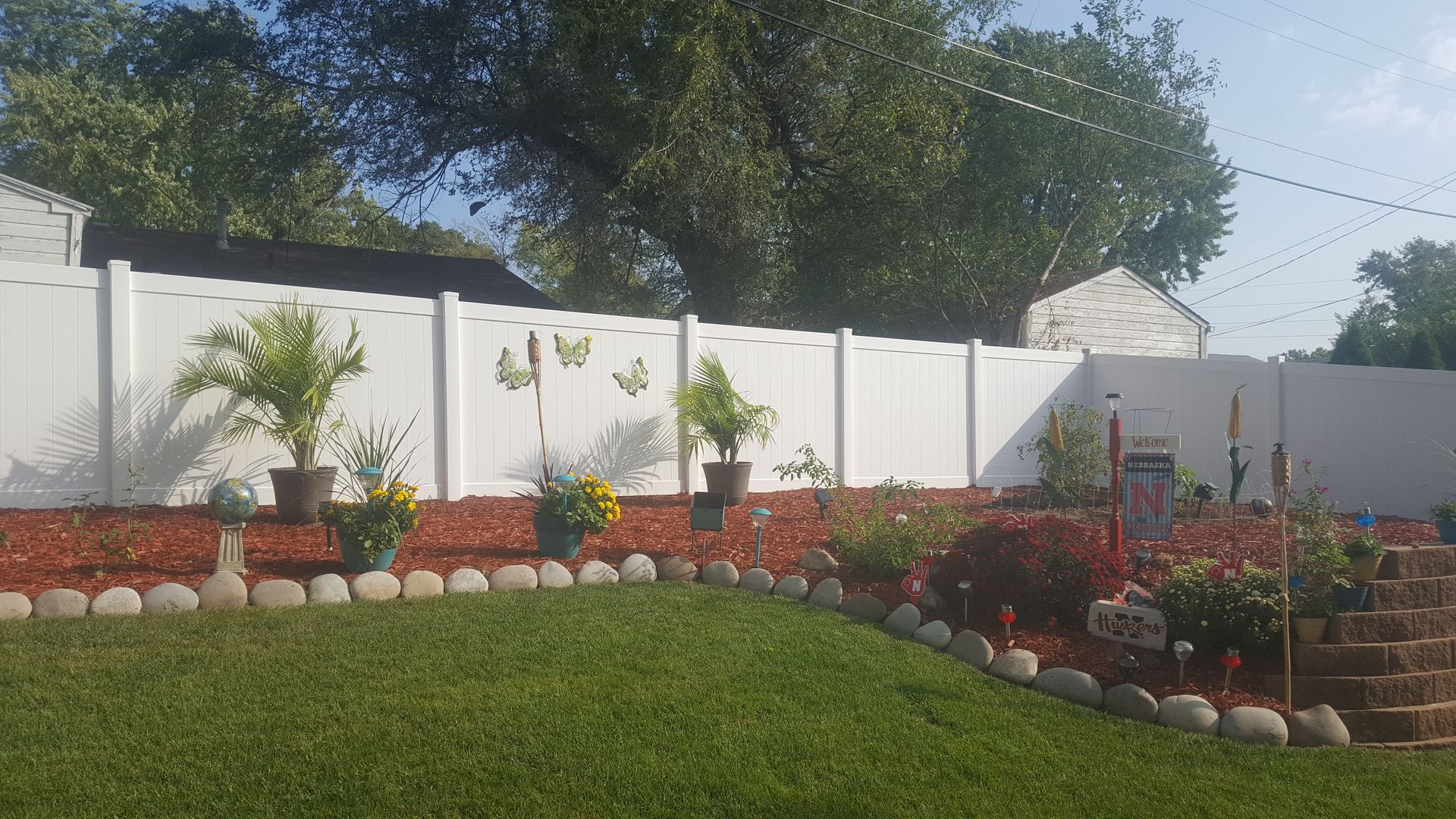 White vinyl fence in a backyard garden with lawn and potted plants.