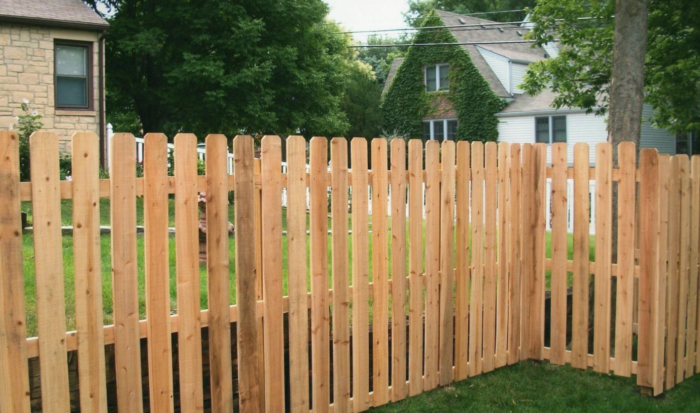 Wooden picket fence in a yard, with houses and trees in the background.