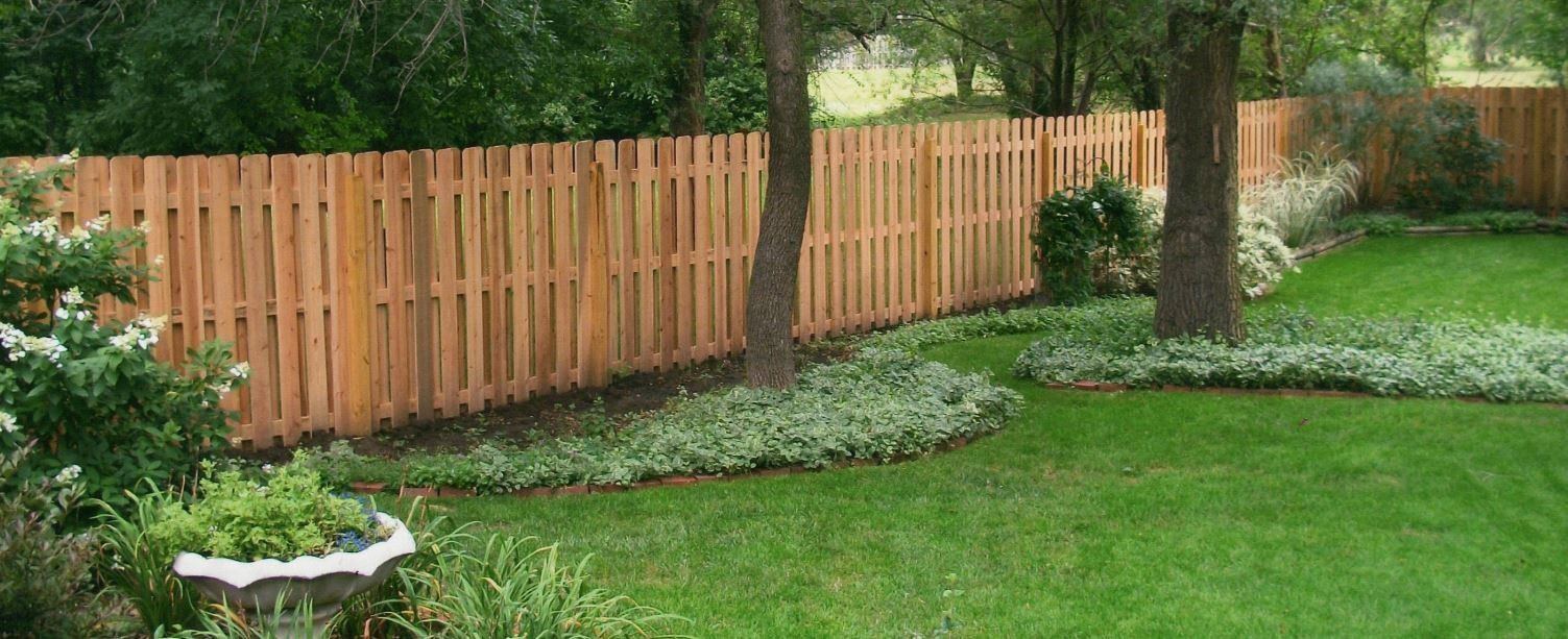 Wooden fence in a backyard with lush green grass and trees.