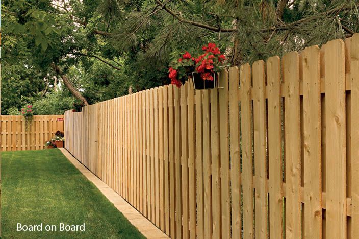 Wooden board-on-board fence in a green yard, with a hanging flower basket, trees in the background.