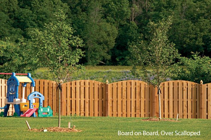 Wooden scalloped fence encloses backyard with trees, green grass, and a colorful playset.