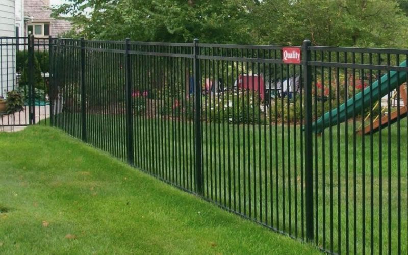 Black metal fence encloses a green lawn, with a slide visible behind it.