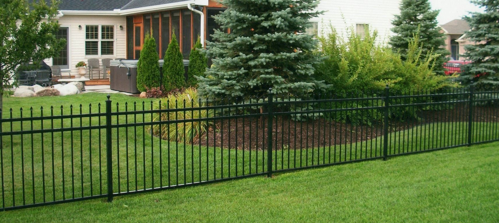 Black metal fence in a grassy yard, with house and trees in the background.