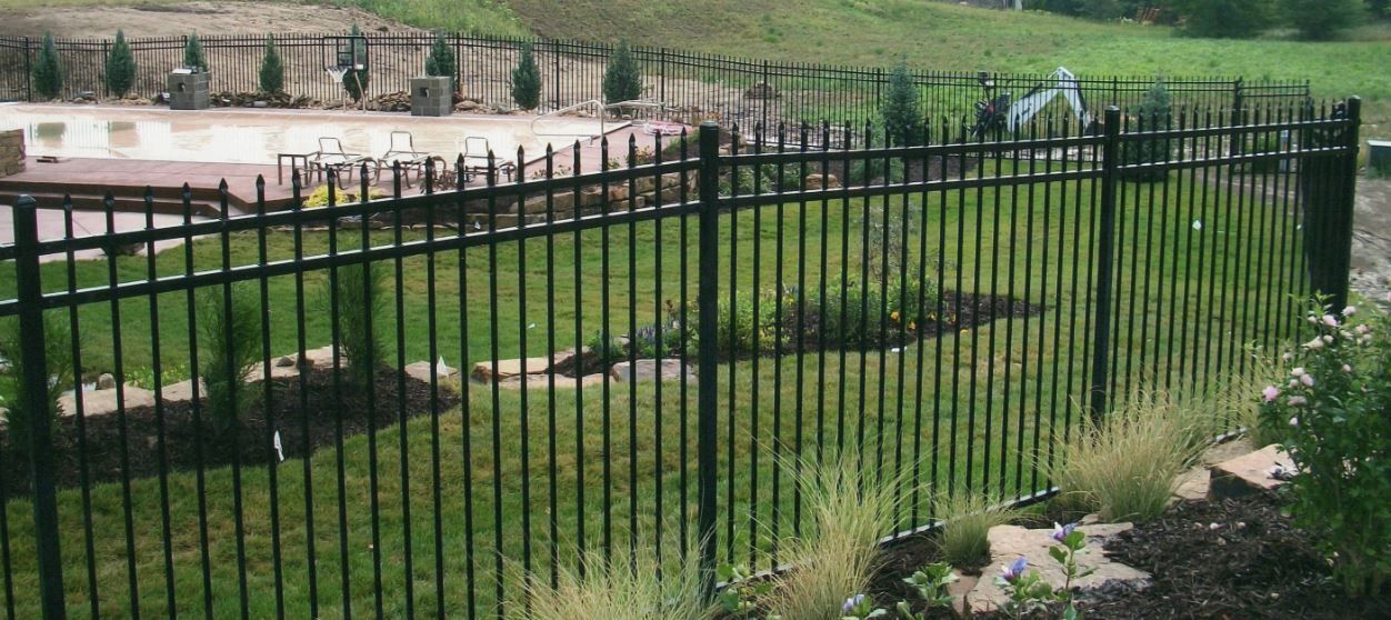 Black metal fence in a yard with green grass and some landscaping.