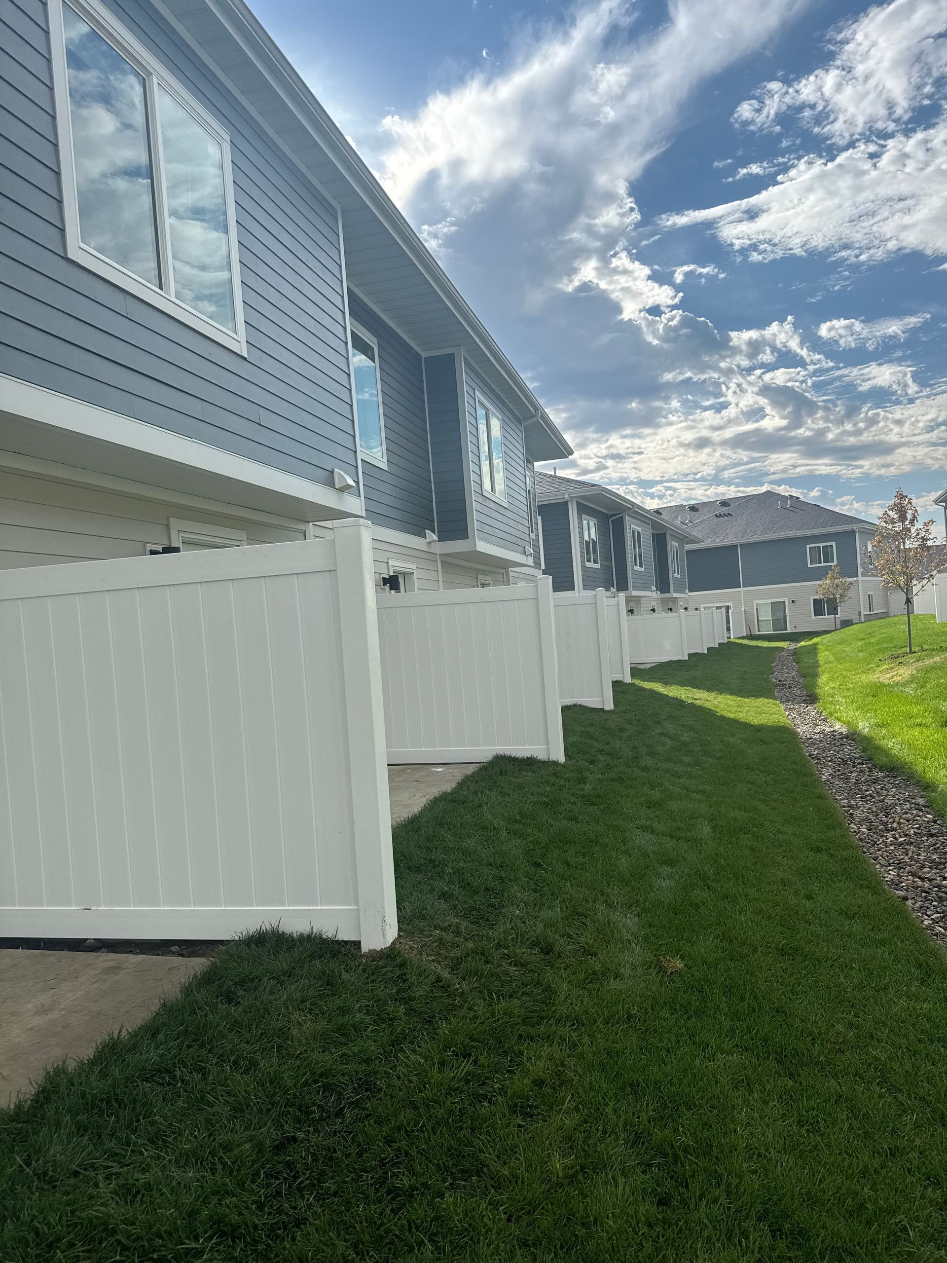 Row of townhouses with white fences and green grass under a partly cloudy sky.