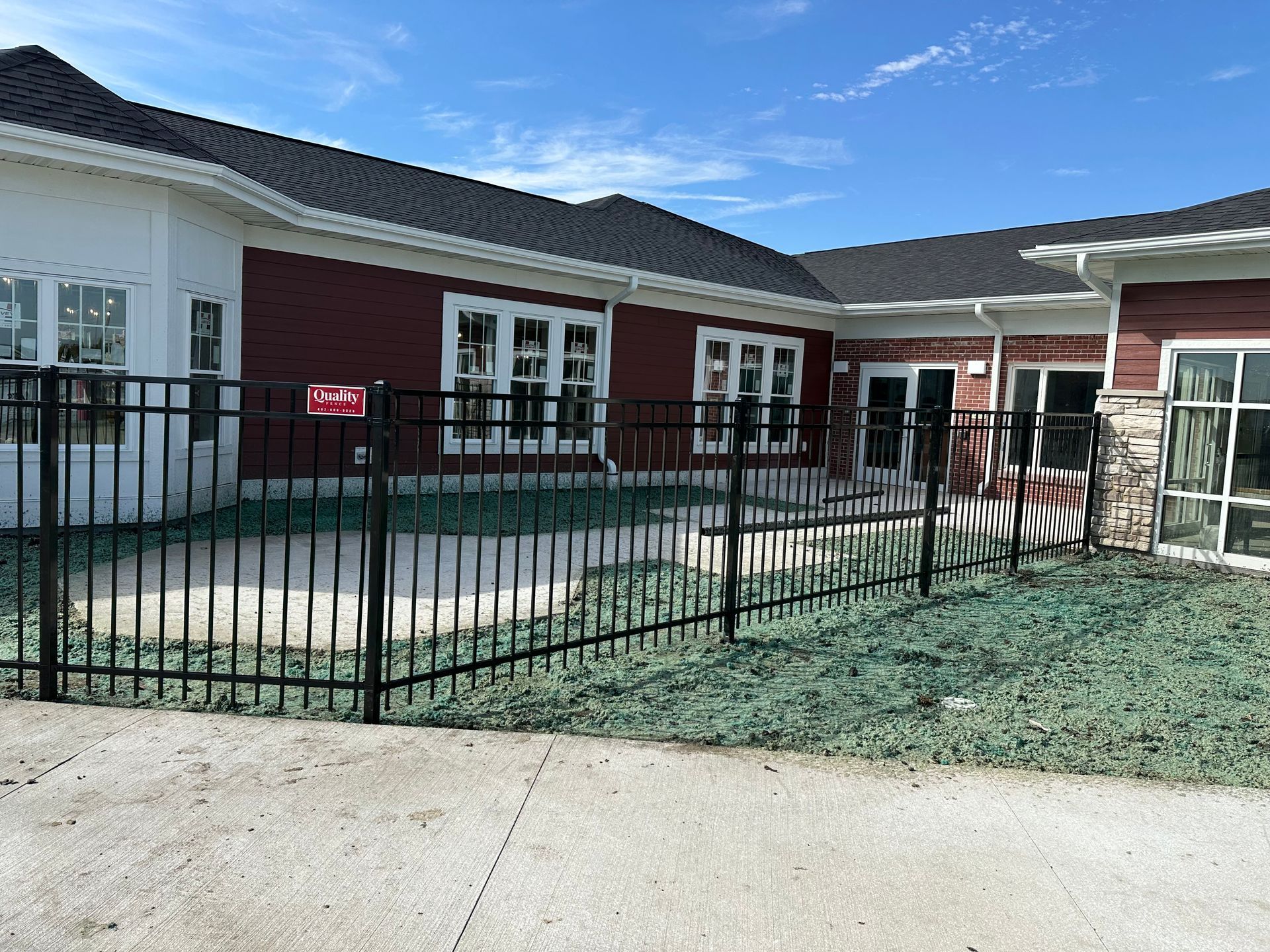Black metal fence in front of a building with red and tan siding, windows, and black roof, under a blue sky.