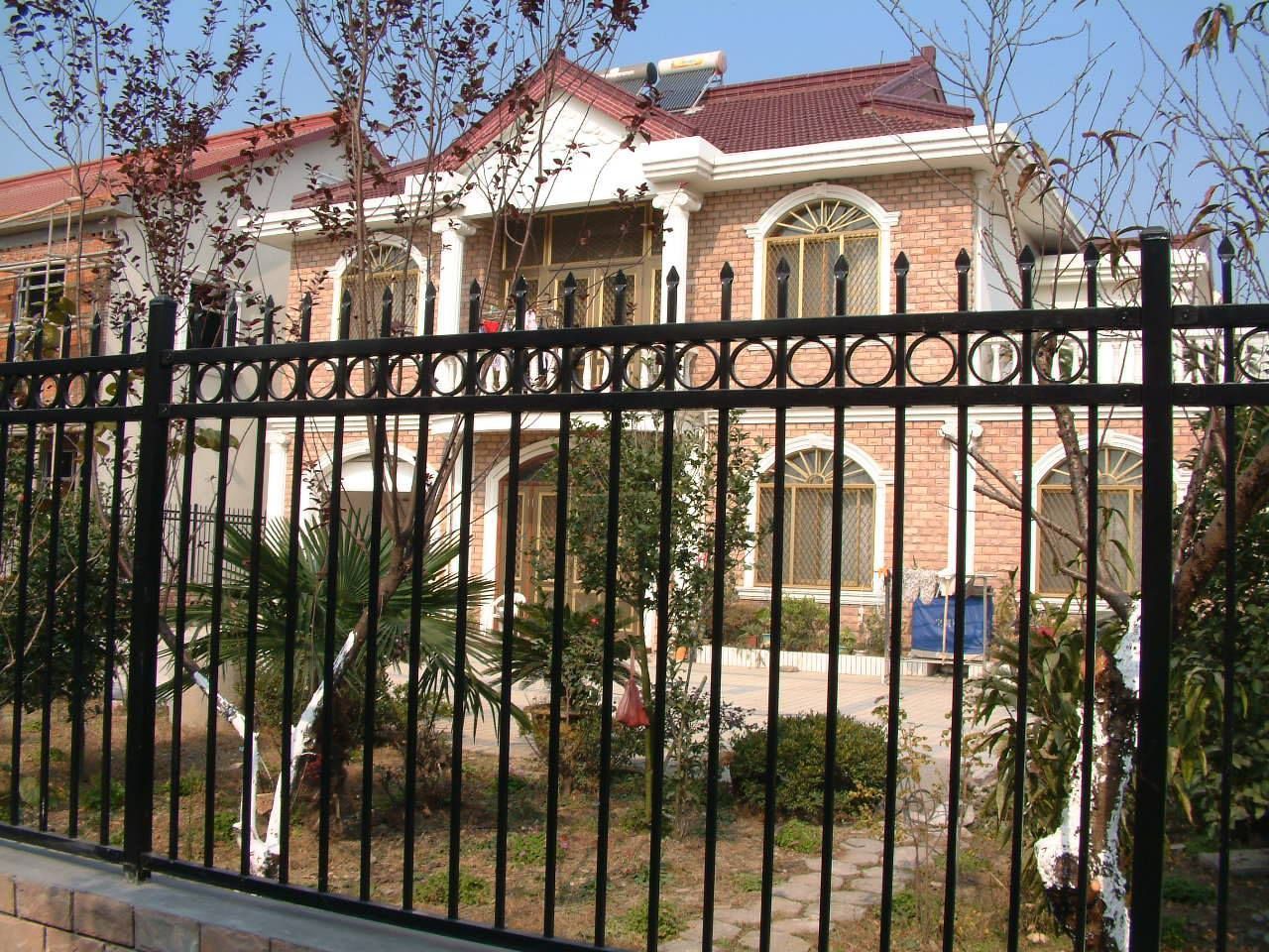 Black metal fence in front of a two-story brick house with a red tile roof and white trim.