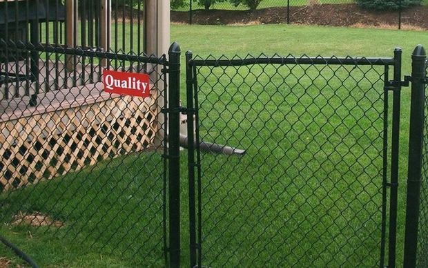 Black chain-link fence with a gate, green grass, and a red "Quality" sign.