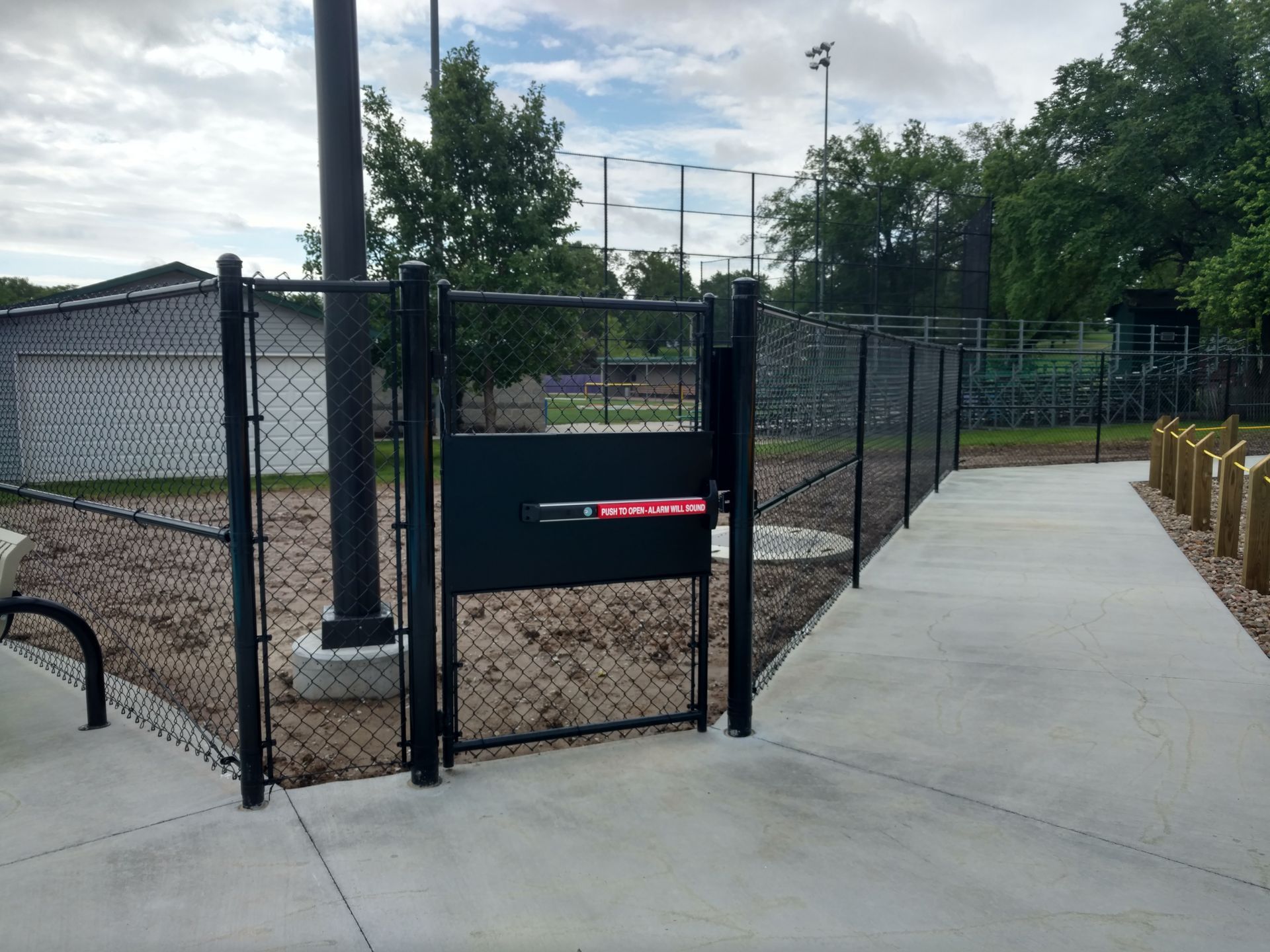 Black chain-link fence with a gate, leading to a concrete path. A sign reads 
