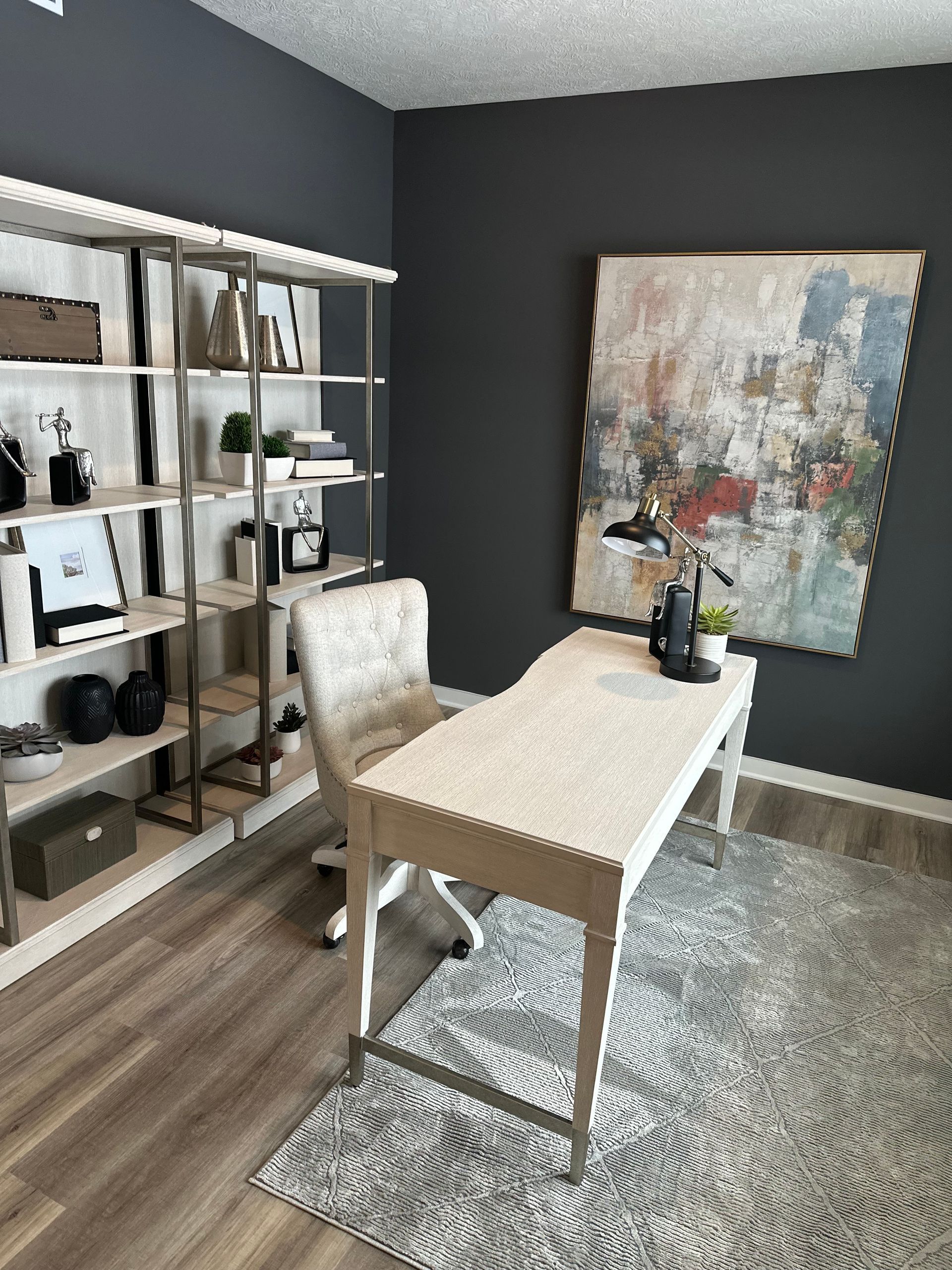 A home office with a desk , chair , shelves and a painting on the wall.