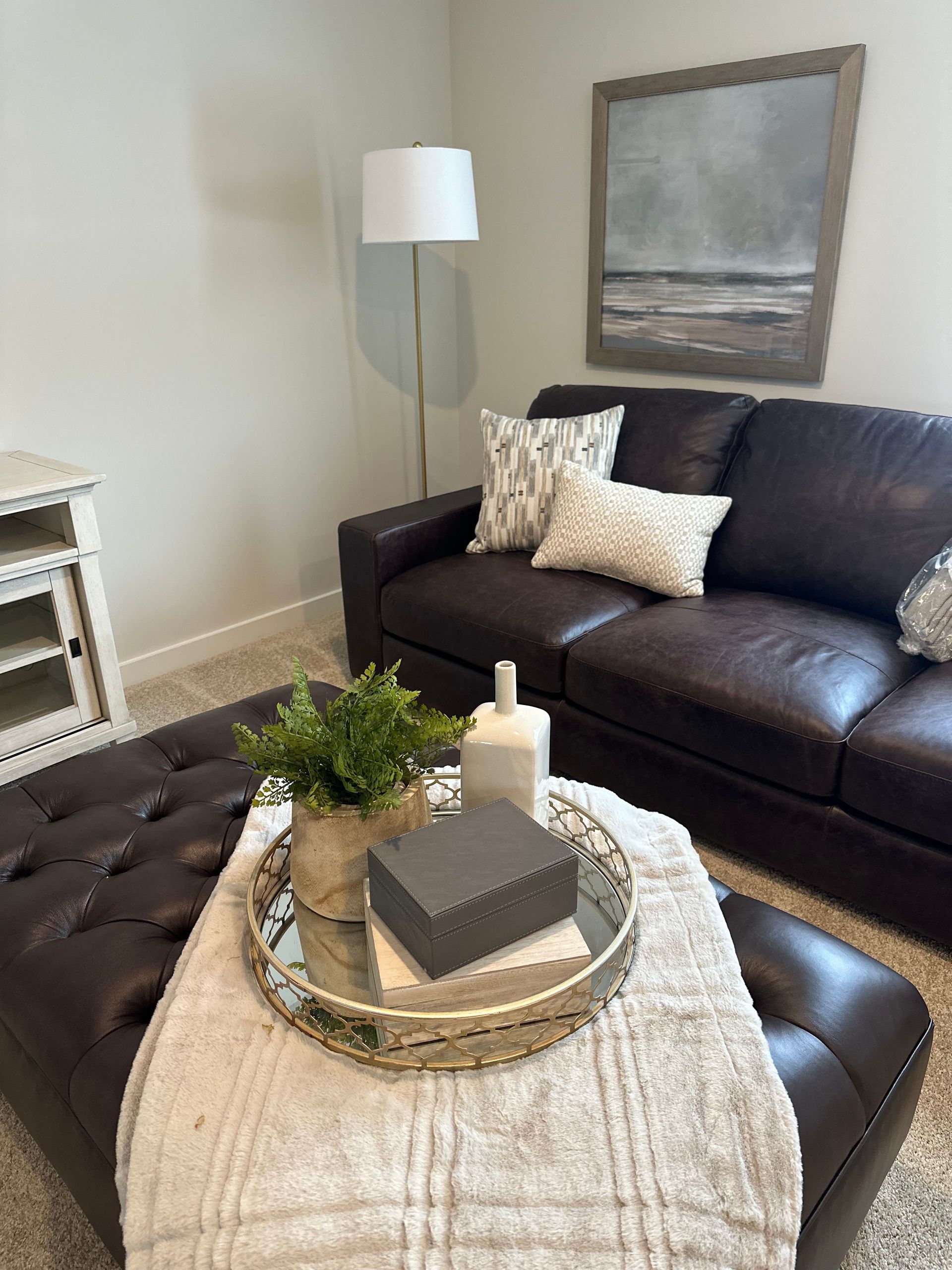 A living room with a couch , ottoman , coffee table and lamp.