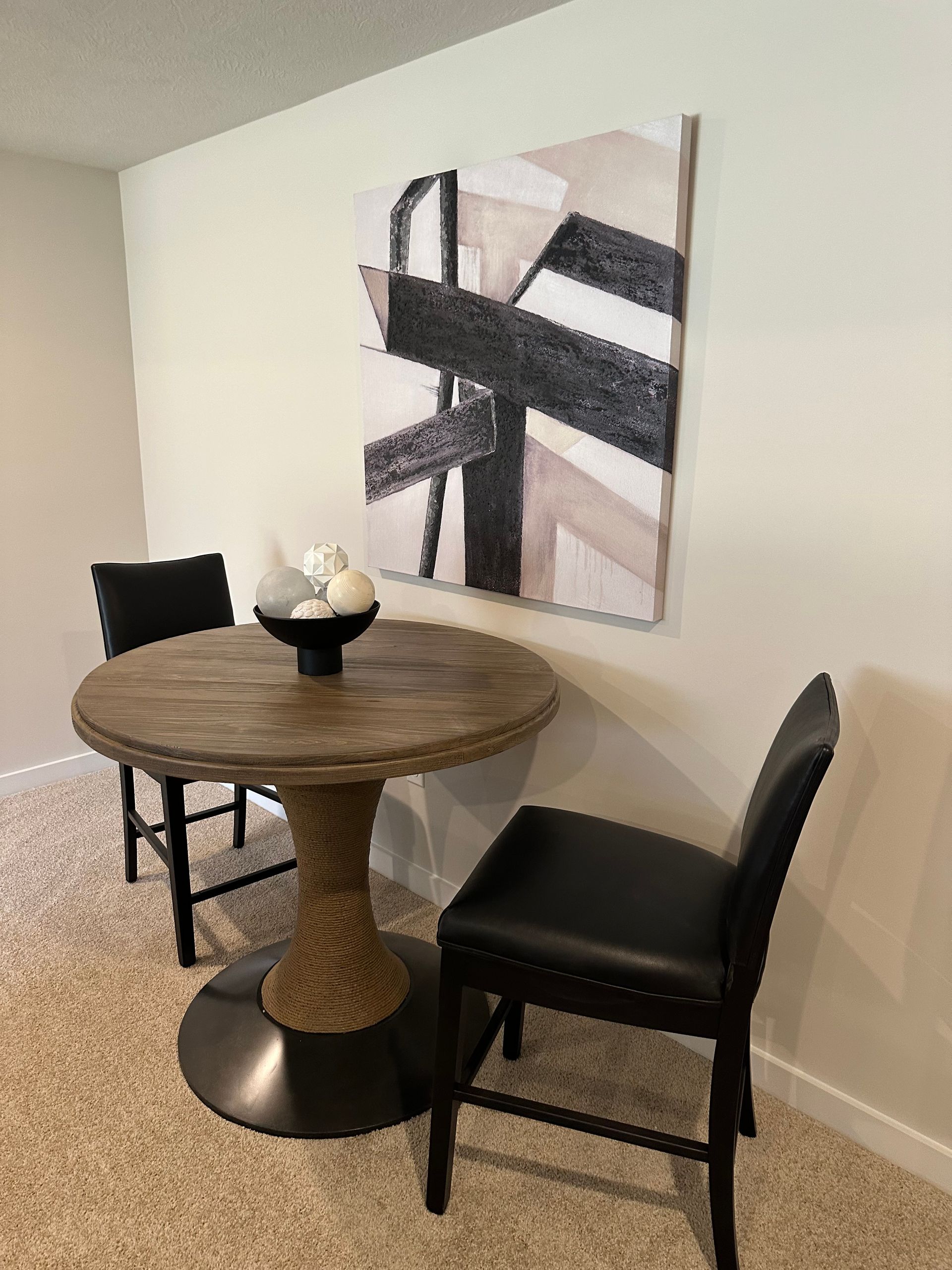 A dining room with a table and chairs and a painting on the wall.