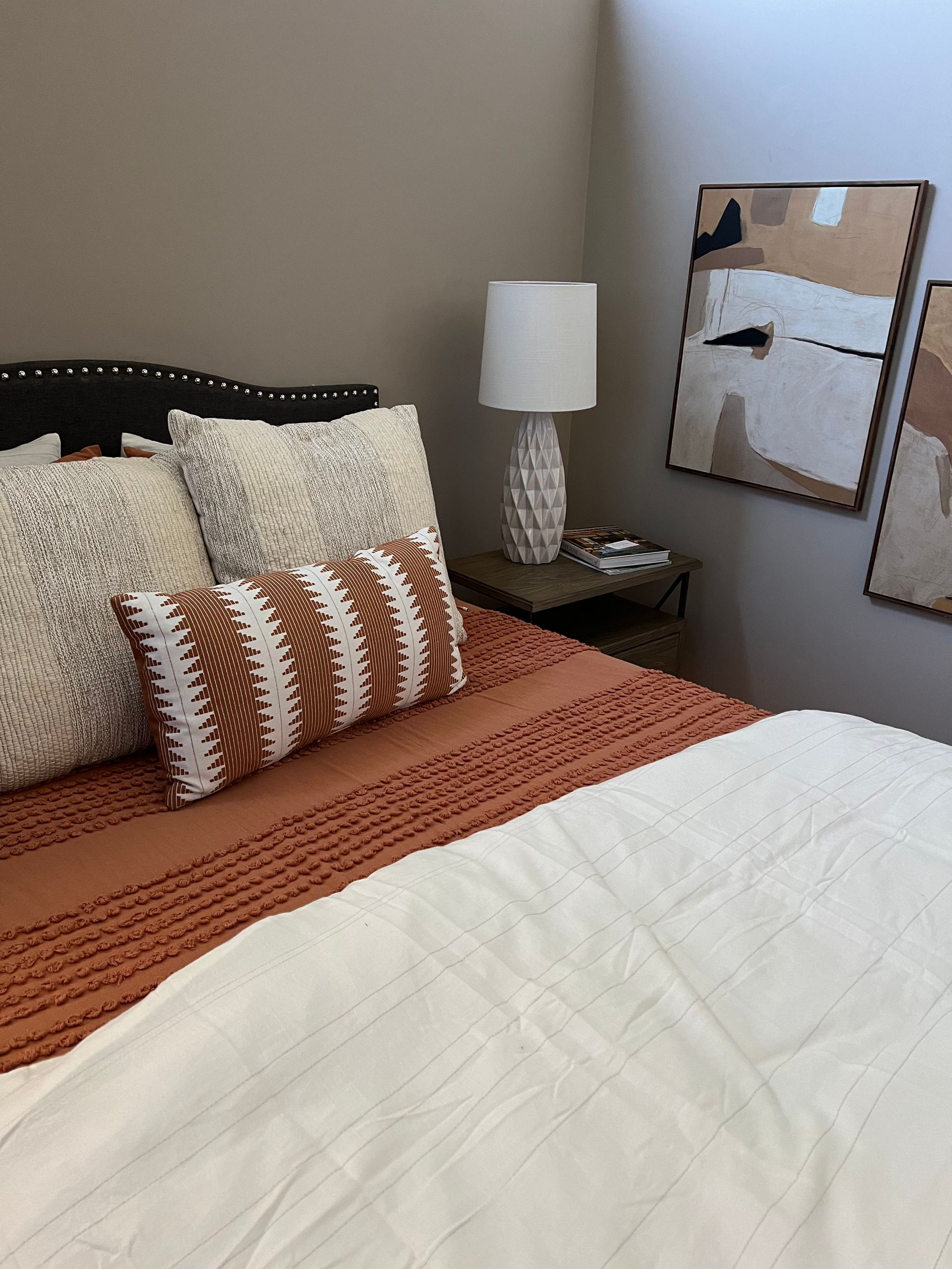 A bedroom with a bed, lamp, and two paintings on the wall.