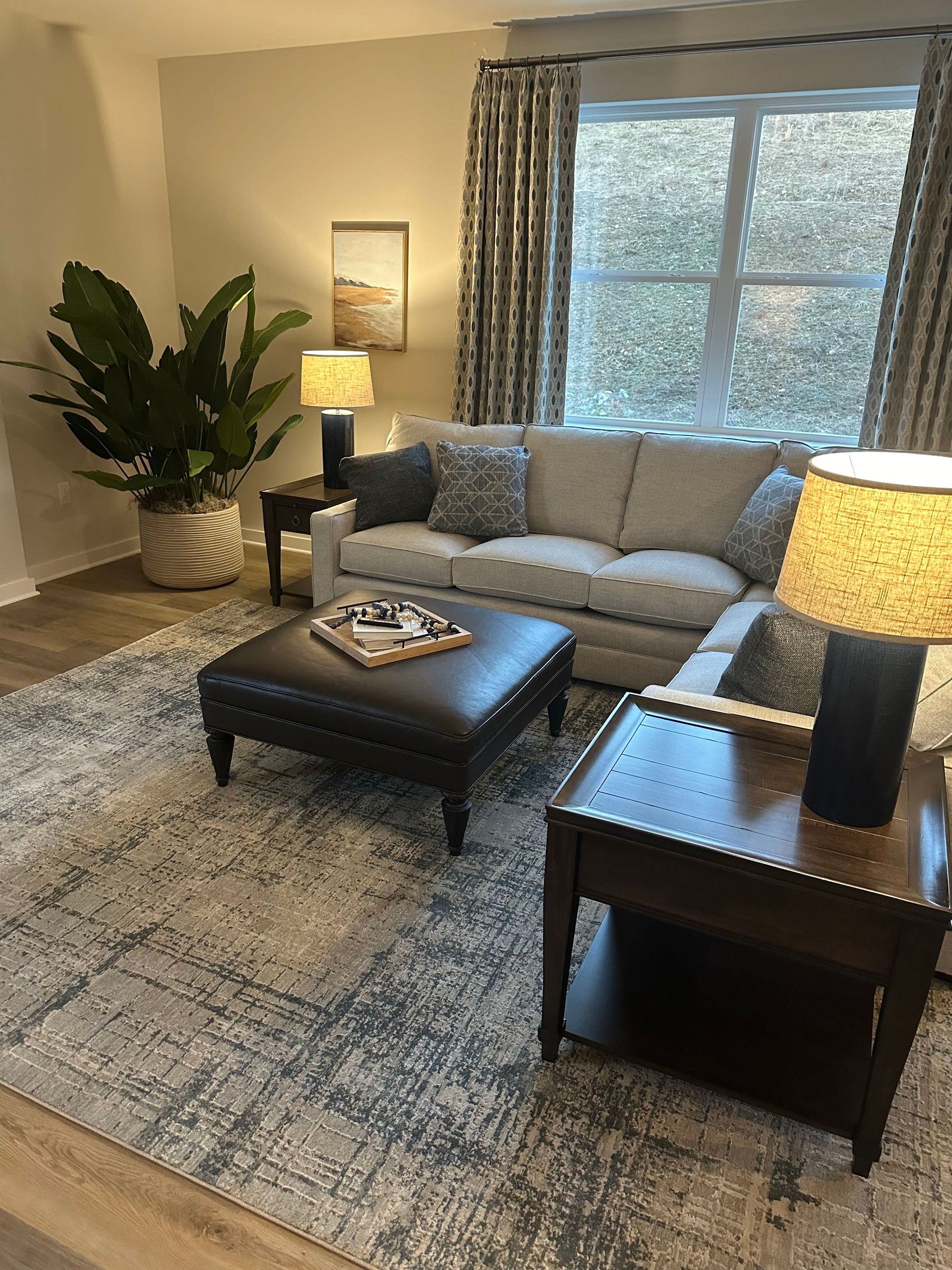 A living room with a couch, ottoman , lamps , and a rug.