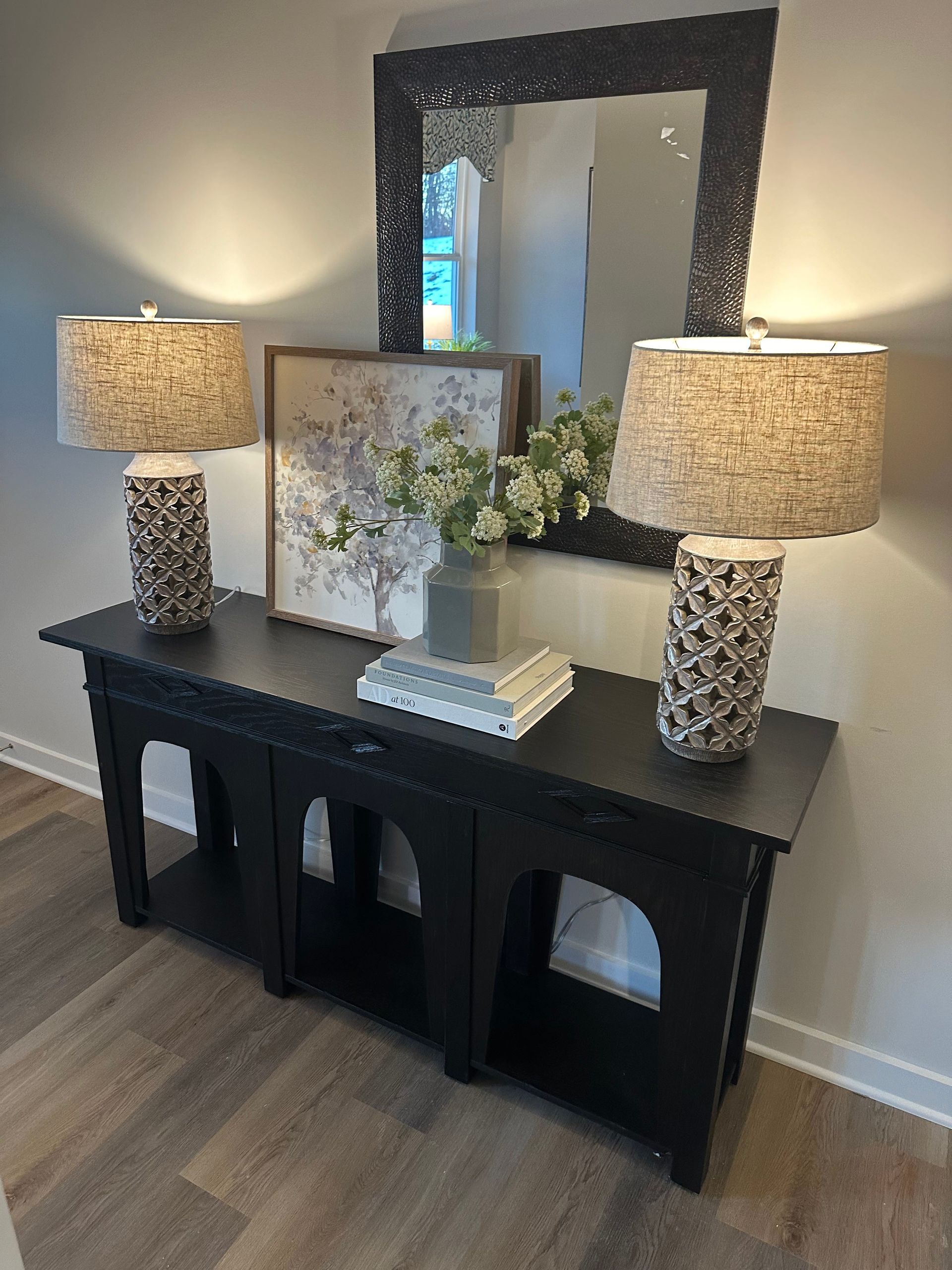 A black console table with two lamps and a mirror in a living room.